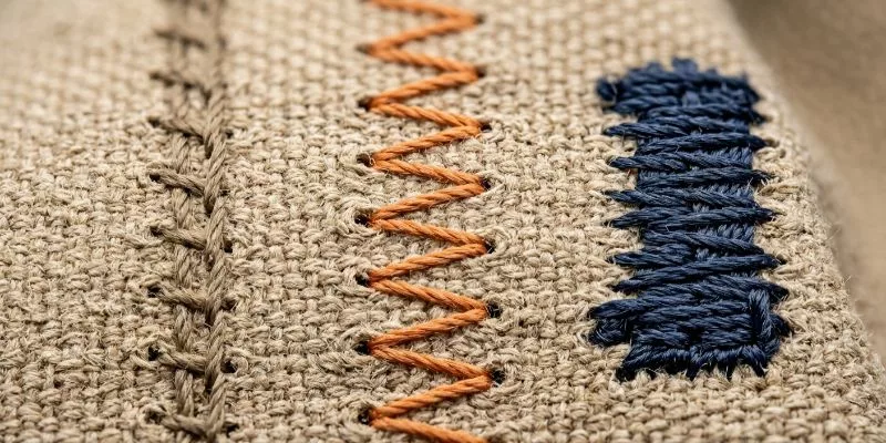 Macro photography of physical thread loops including lockstitch, zigzag, and bar tack on canvas fabric.