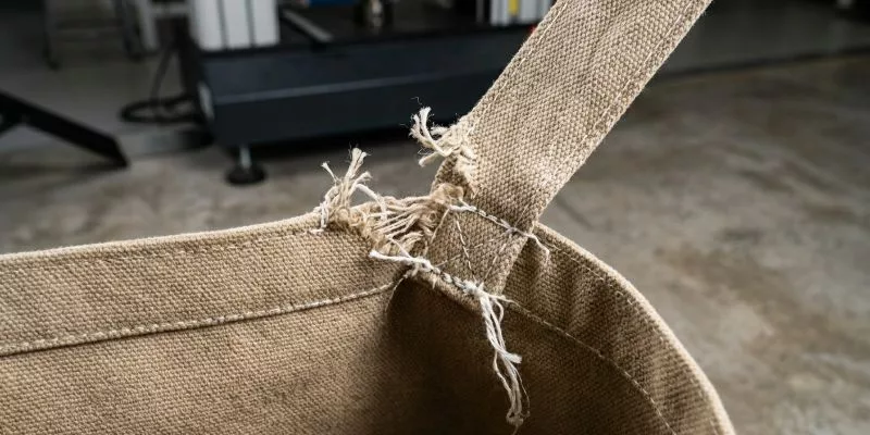 Close-up of a torn handle seam and snapped nylon thread on a tested 12oz canvas bag.