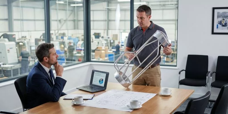 OEM factory engineer presenting a high-quality aluminum golf bag frame to a brand client during a business meeting