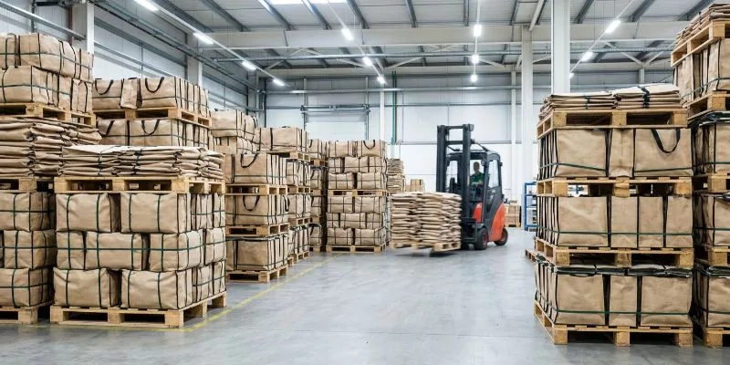 Pallets of custom retail tote bags ready for shipping in a busy factory warehouse, demonstrating massive production scale.