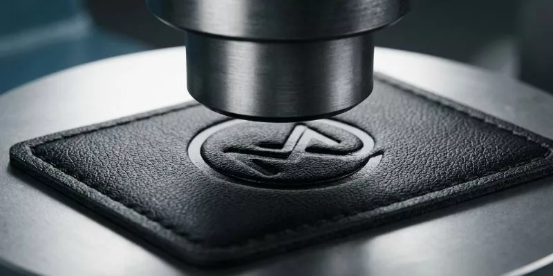 High-frequency debossing machine pressing a corporate logo onto a synthetic leather backpack patch