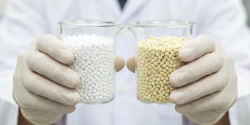6. Engineer holding two glass beakers comparing raw white polymer resin and yellow UV stabilizer additives.