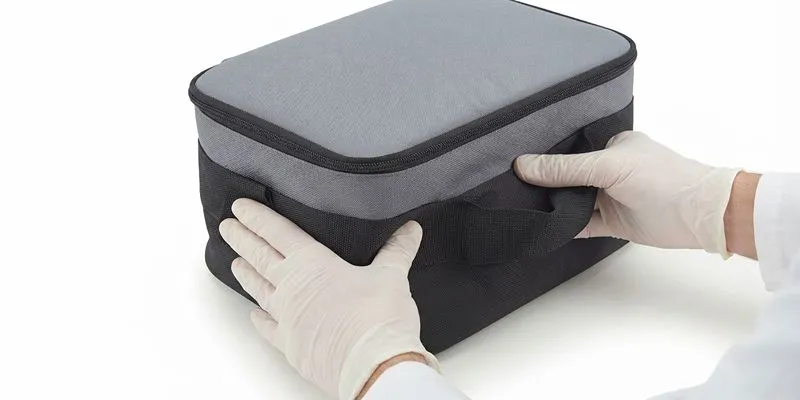 Gloved hands inspecting the corner seam of an insulated lunch bag during troubleshooting
