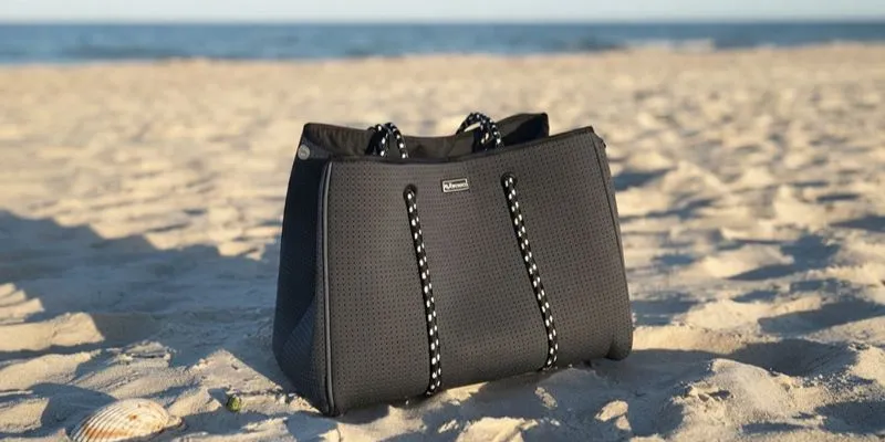 Black perforated neoprene beach tote with rope handles on the sand