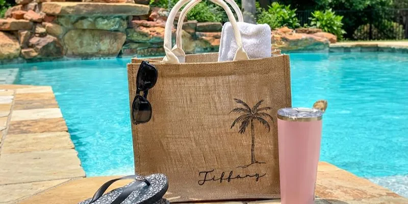 Natural jute beach tote with a palm tree print beside a pool