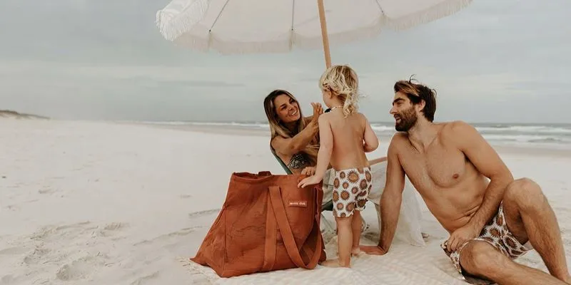 Oversized family beach bag filled with towels on the sand under a beach umbrella