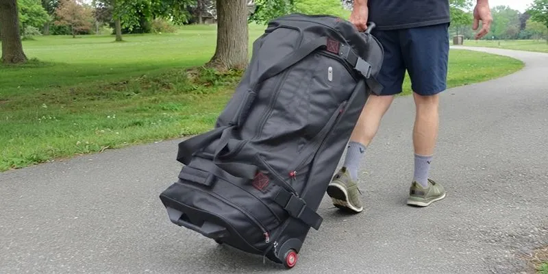 Rolling duffle bag with a telescoping handle and wheels pulled along a path