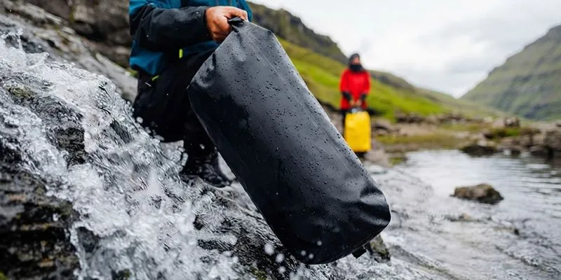 Waterproof dry duffle with welded seams carried through a waterfall stream