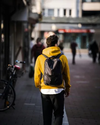 Man with yellow and black backpack walking on city sidewalk