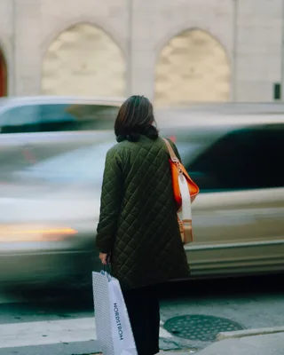 Woman with shopping bag crossing street with blurred cars